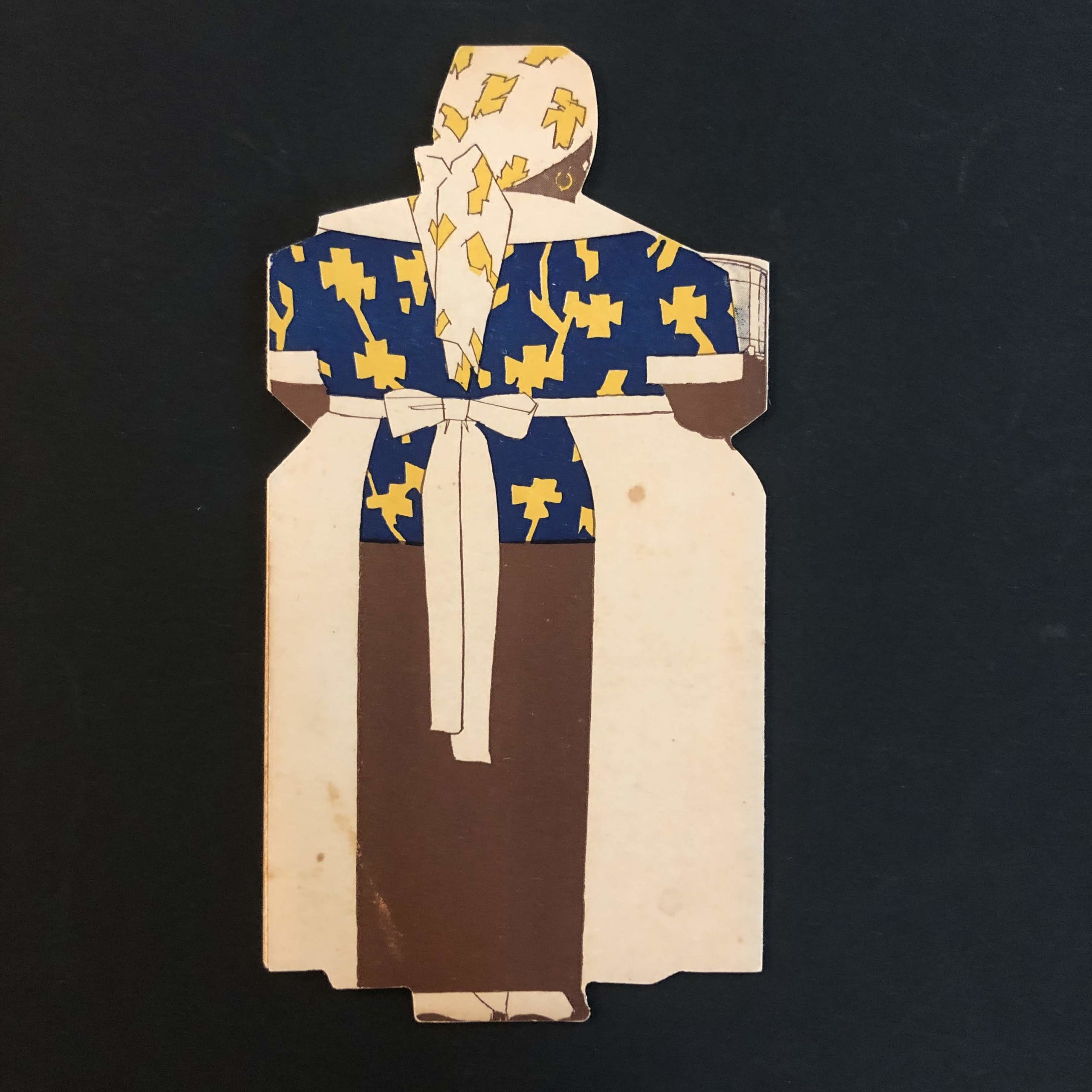 Photograph of back of a trade catalog in the shape of a woman with dark skin wearing a kerchief over her head and a large white apron.