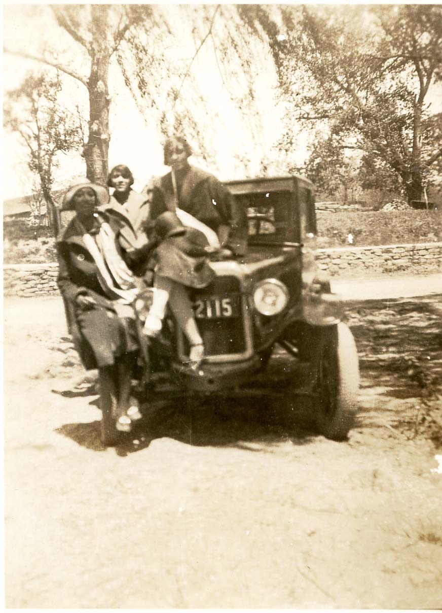 An early 20th century image of three women sitting on a car.