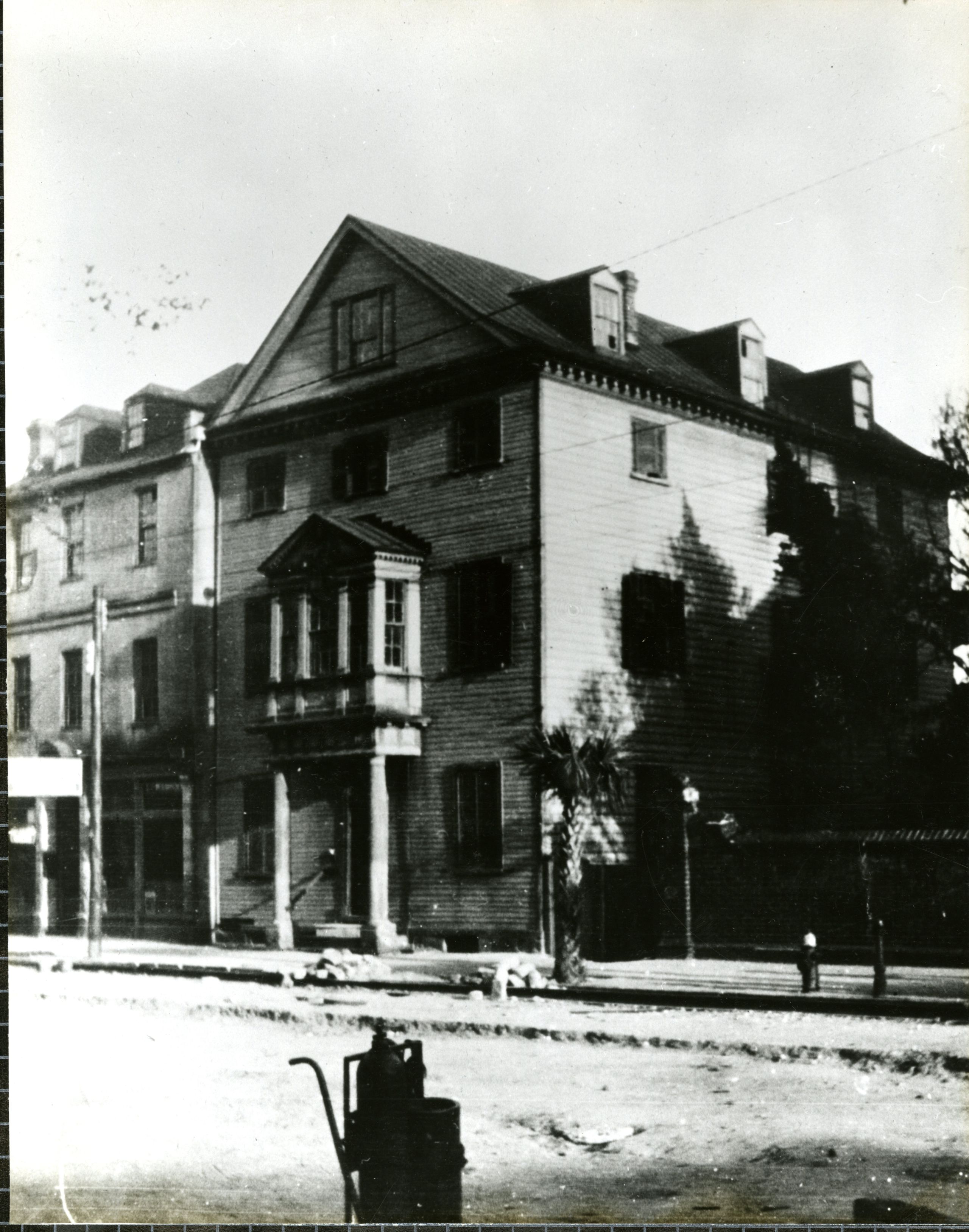Black and white 1920s image of a large house next to a road.