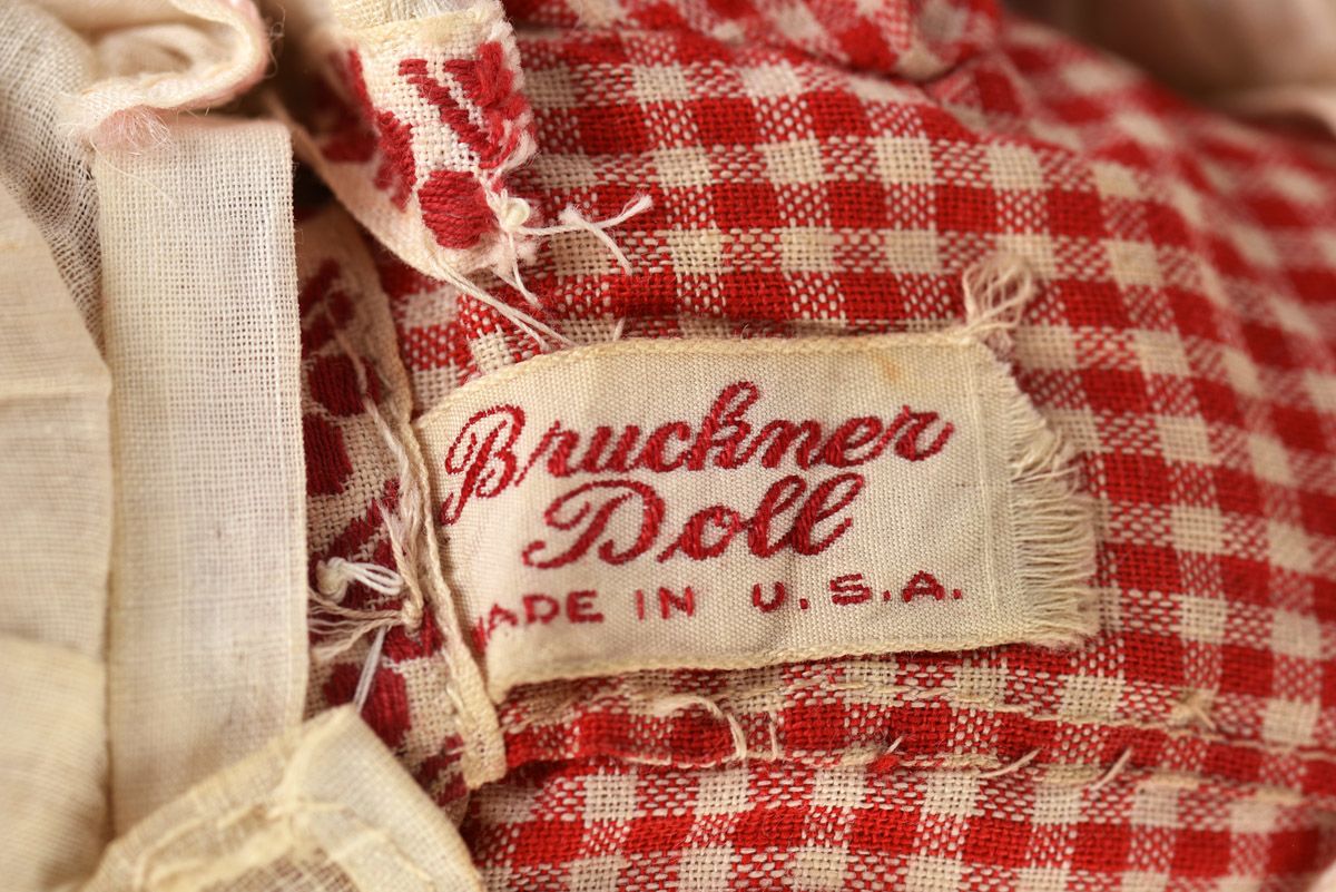 A piece of red and white gingham fabric with a tag. The tag reads Bruckner Doll, Made in U.S.A.
